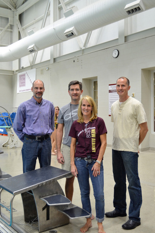 Industrial Design, Group of four pose around starting block for photo smiling, swimmers mill about in the background