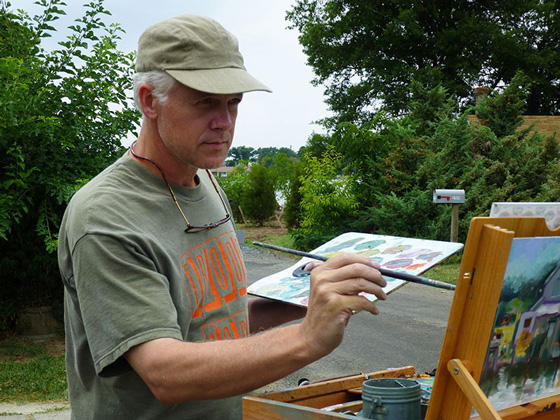 Fine Arts, Christopher painting on wooden easel outdoors in a baseball cap and thsirt, against a lush background of grass and trees