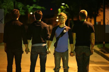 Film & Video, Still image from The Felis Culpa, image of four men holding hands in the middle of a street at night, man second from right faces forwards while other three face opposite direction