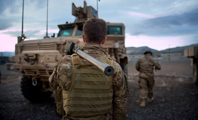 Photography, Image of soldiers in uniform near military vehicle, in the forground a soldier's back is to the camera with a metal pip resting over his shoulder