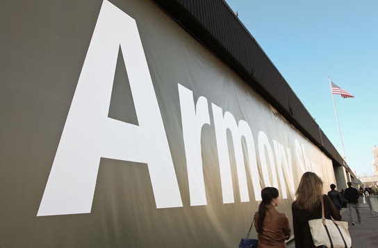 Fine Arts, image of people walking along side walk next to a massive black banner with white text that reads "Armory"