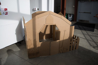 Interior Design, Photo of cardboard model of child's play house, side featured depicts a farm house with raised detail of crops and a shovel