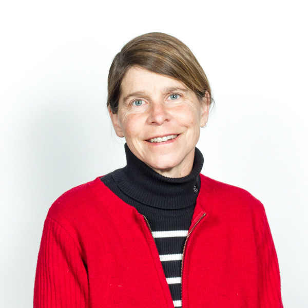 Headshot of Carol Boram-Hays, smiling, in black and white striped sweater with red jacket, against a white background