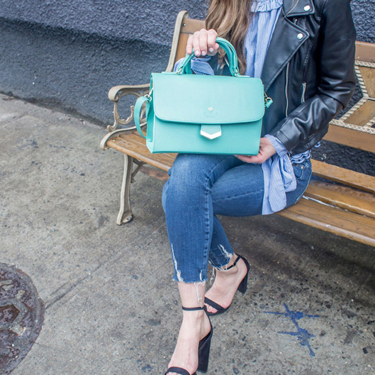 Industrial Design, model from neck down sitting on bench displaying blue hand bag to camera