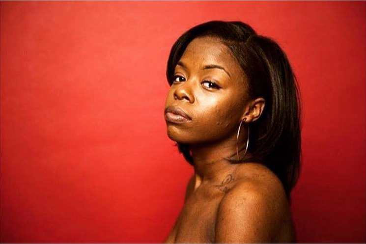 Photography, Headshot of Jamilla Kato, three quarter facing camera, not smiling, from the shoulders up against a red backdrop