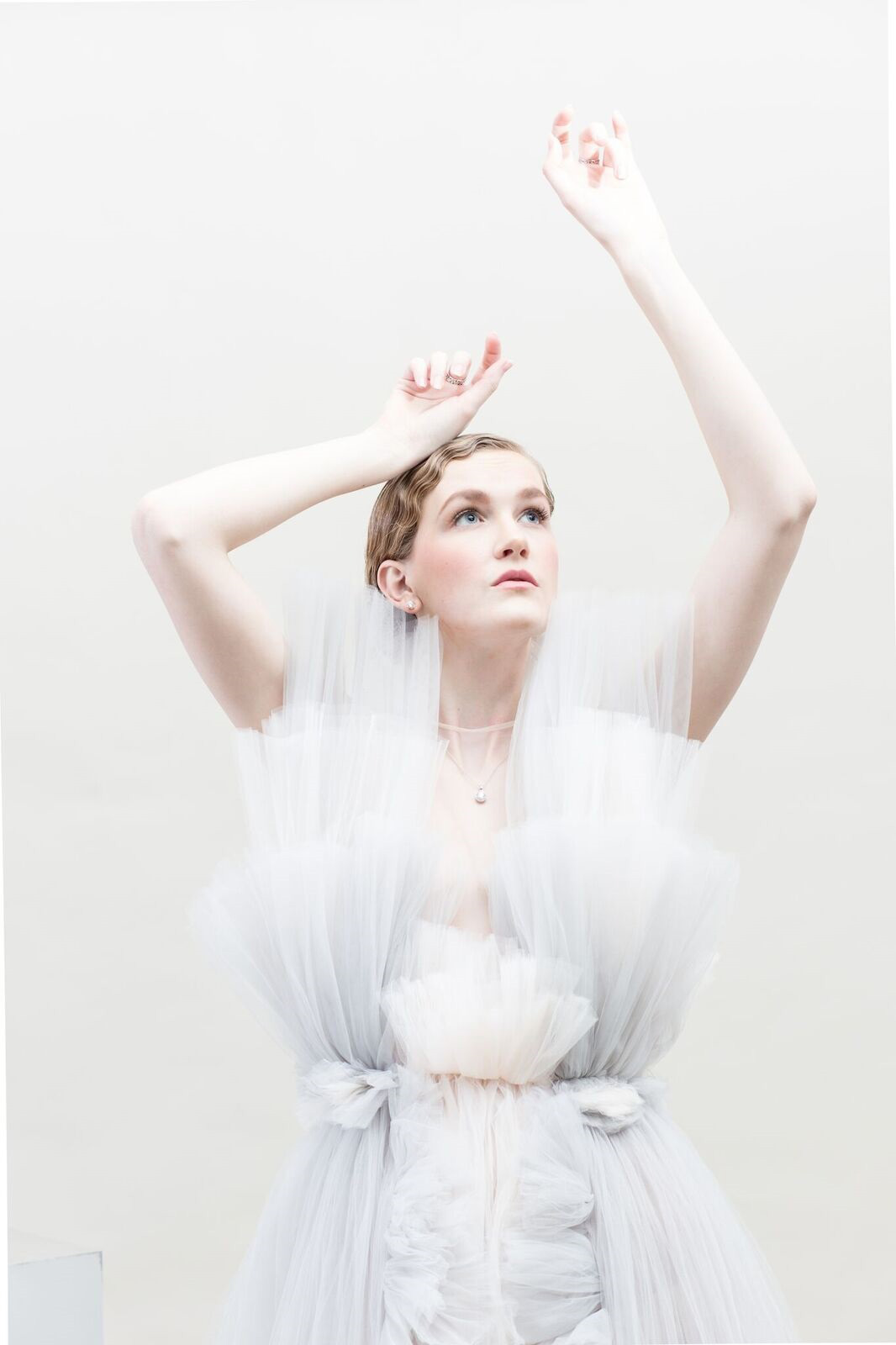 Fashion Design, Model in pastel tulle garment by Jennie Moon posing, looking up towards light with arms raised