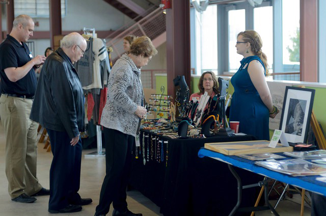 Master of Fine Arts, Image of Carmen Smith at Art Fair interacting with guests at her table near the stairs in the lobby of Crane