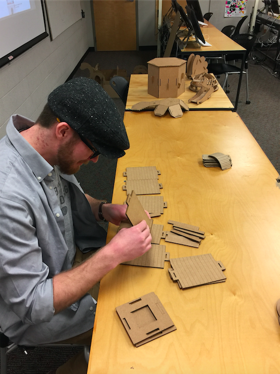 Animation, student works at table to piece cardboard structure together