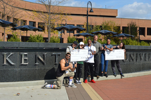 Life at CCAD, Winners of Sky Hack Aviation Hackathon stand in front of Kent State University Sign holding two giant checks