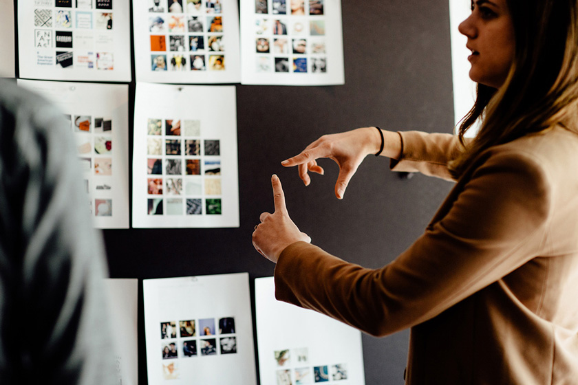 Advertising & Graphic Design, Danielle Delay from Ologie standing in front of inspiration board full of pinned pictures, talking and gesturing with hands to someone partially out of frame