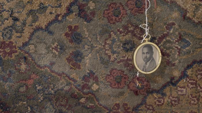 Fine Arts, Photo of open locket with black and white photo of a man hanging from white string in front of ornate rug