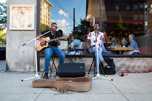 Life at CCAD, Photo of musicians playing in the short north in front of restaurant window reflecting buildings and a blue sky