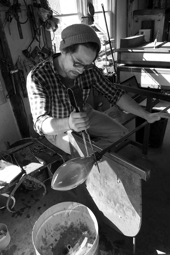 Fine Arts, Black and white image of matthew working with blown glass and tools, surround by glass blowing equipment