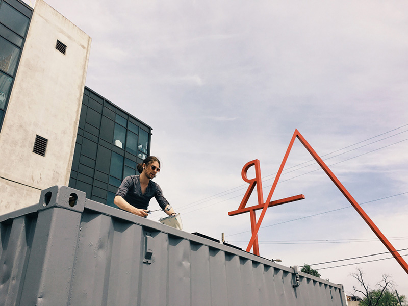 Industrial Design, Photo of Katz working on top of the shipping container, shot from below, with art sign visible in background. 