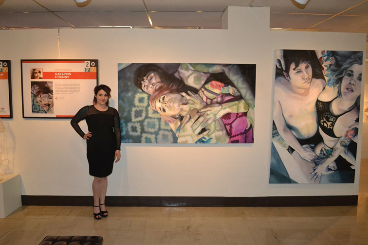 Fine Arts, Kaylynn Etienne in black dress posing with large paintings hanging on white gallery wall