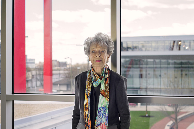 Life at CCAD, Loann Crane poses in front of window looking out on the Art Sign and the Loann Crane Center for Design