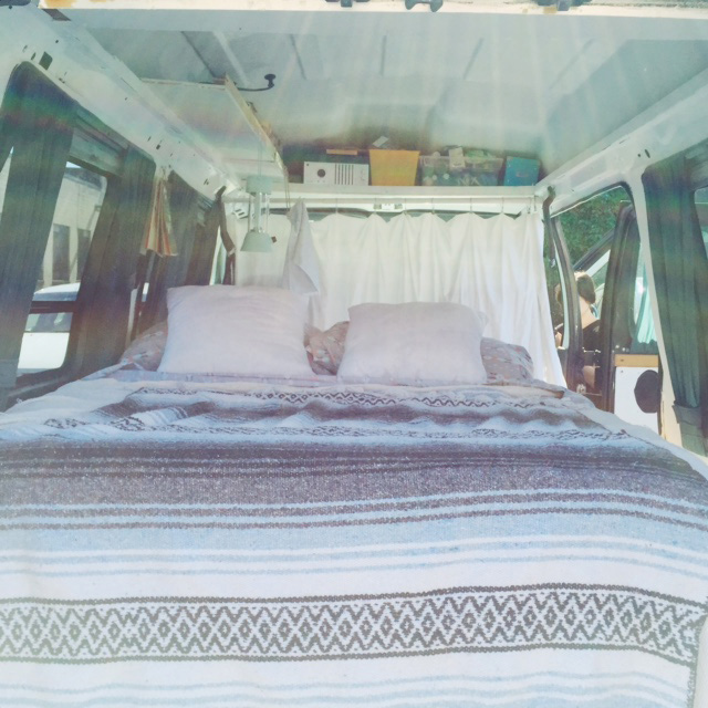 Illustration, photograph of bed in camper van, in the background a white sheet separates living area from drivers cab.