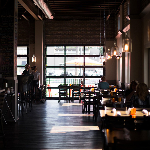 Life at CCAD, Photo of dark interior where people sit at cafe tables with window overlooking street in background at Lomonico's near CCAD