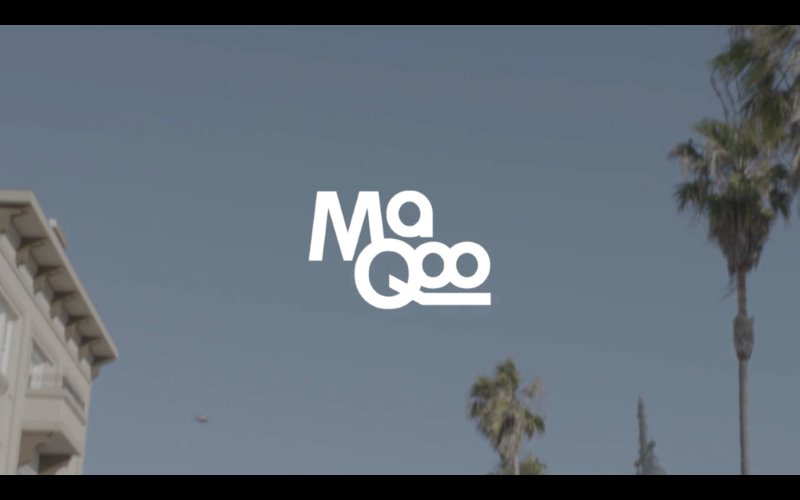 Fine Arts, Image of blue sky featuring corner of building and palm tree with white overlaid text logo which reads "MaQoo"