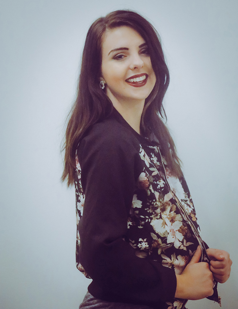 Fashion Design, Headshot of MollyKate in floral racing jacket, body facing away from camera smiling, against a white background