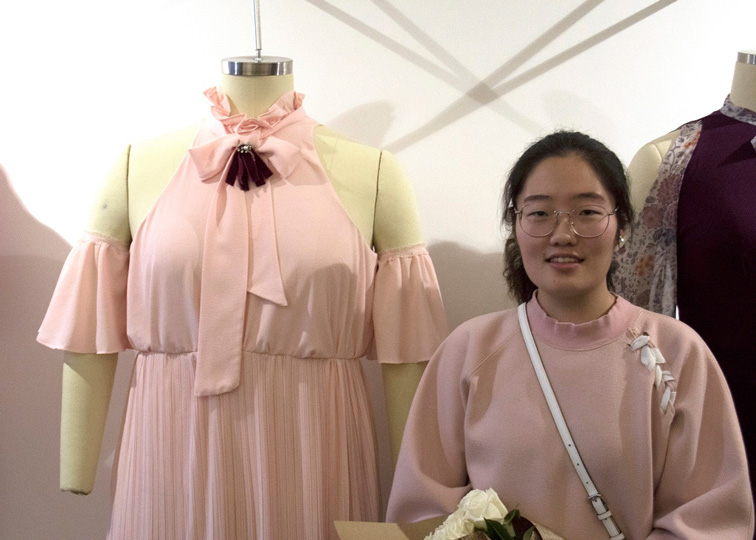 Fashion Design, CCAD Fashion Design student Ran Tao's winning design for Eloquii, Ran Tao in pink sweater posing with mannequin sporting a pink dress