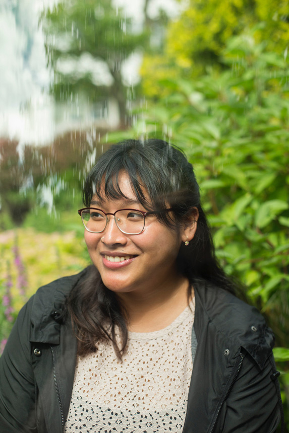 Life at CCAD, Headshot of Sanne Sok standing in front of backdrop of trees and flowering plants (Illustration, 2019)