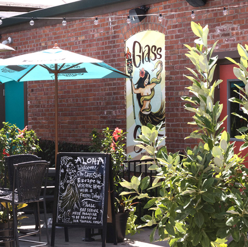 Life at CCAD, Image of lush greenery, tables, and sandwich board with background of brick wall and string lights at Grass Skirt near the CCAD campus