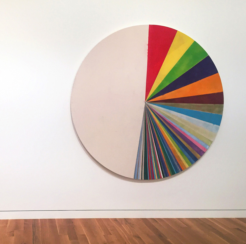 Fine Arts, CCAD Professor Tim Rietenbach's Us, Large wooden circle with colorful slivers painted on top hanging on a white gallery wall with wooden floors.