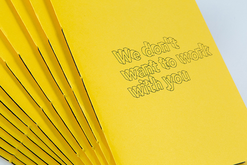 Advertising & Graphic Design, slightly spread stack of yellow booklets on a white background, cover reads "We don't want to work with you" in 3D letters