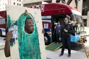 Image of student in front of bus holding up board with painted pickle on it, his face is visible through a cut out oval.