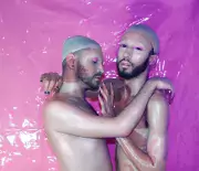 Two models embrace in front of bright pink background