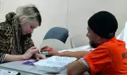 Man and woman work across from one another at table to apply special effects makeup