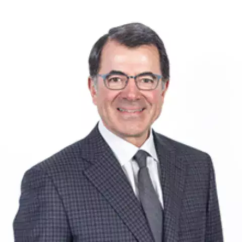 Headshot of Mark Corna in black suit jacket with white shirt and gray tie against a white backdrop.