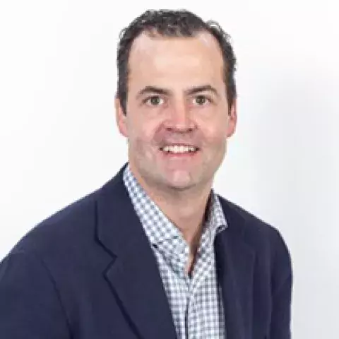 R Blane Walter in navy blue suit and blue and white checkered shirt against a white background.