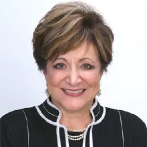 Saundra K. Schuster Esq. in black and white shirt, smiling, against a white background