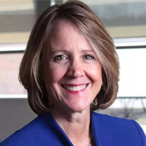 Headshot of Stacia Edwards in blue suit jacket, against a backdrop of a window facing the street outside