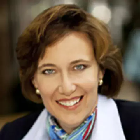 Headshot of Susan D. Rector in black and white jacket with multicolored patterned scarf against a blurred background.