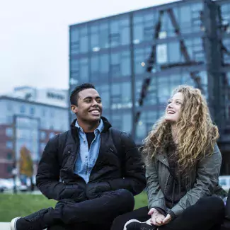 Two students sit on campus green with Art Sign in the background.